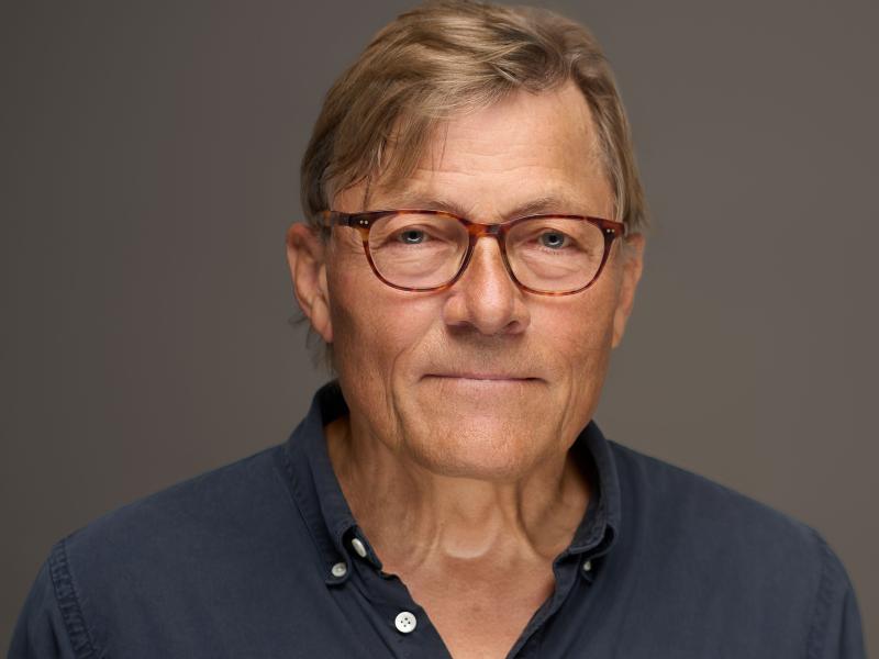 Ole retsbo kigger ind i kameraet. Han er iført en mørkeblå polotrøje og briller.